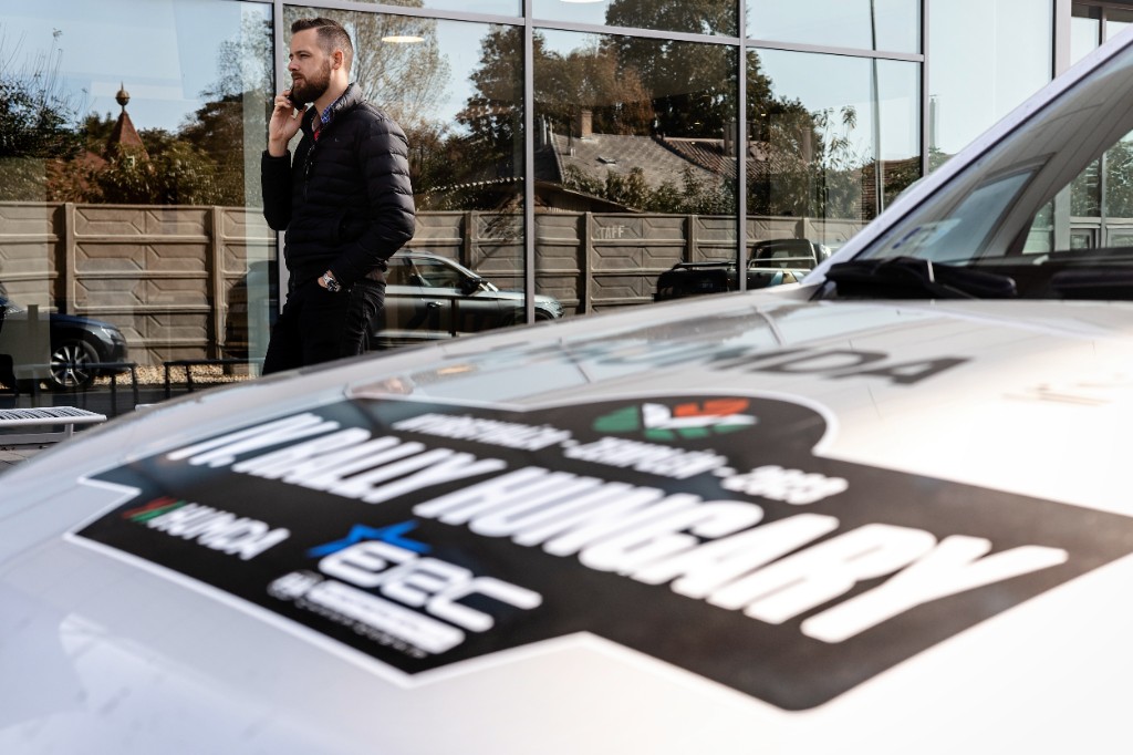 Kornel Ory on a call beside a Rally Hungary branded car
