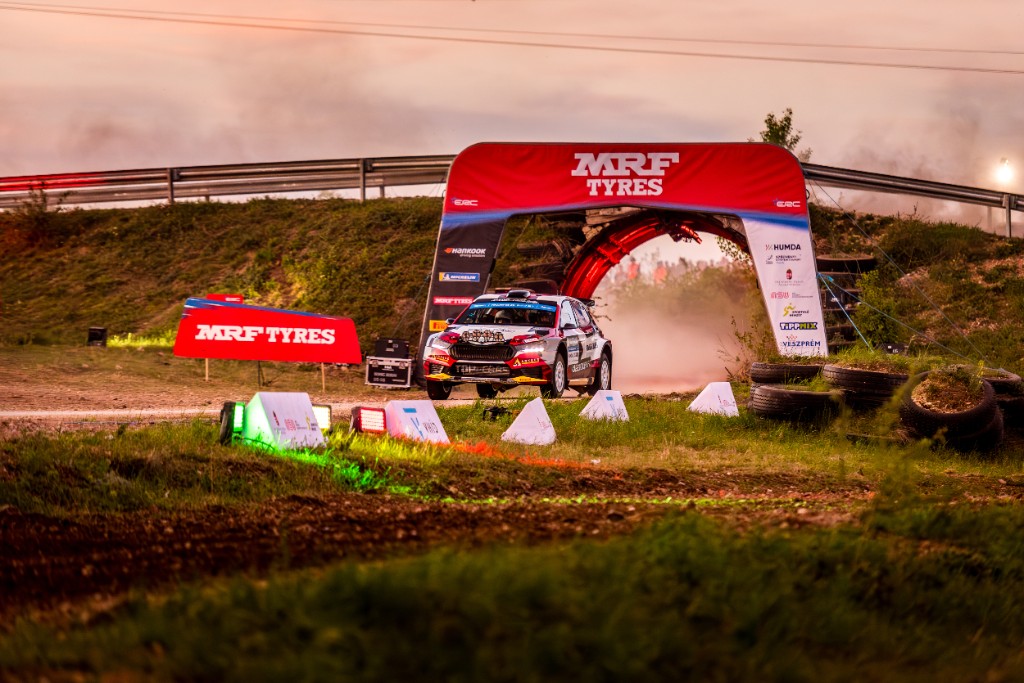 Rally car passing under the MRF Tyres arch at dusk
